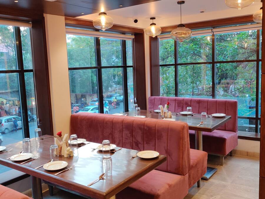 A restaurant with red booths and tables, large windows with a view of the street, and pendant lighting.