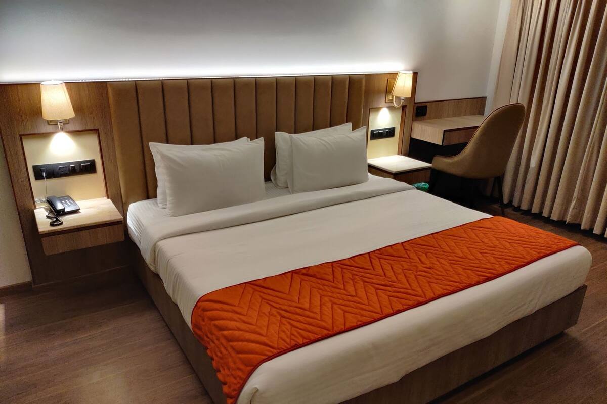 A hotel room with a large bed, two bedside tables with lamps, a chair, and a window with curtains.