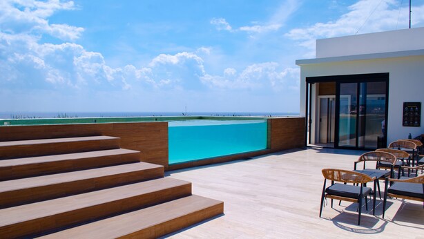A modern outdoor terrace with a pool, wooden steps, and seating area. - Modern Pool View New Condo Gym Jacuzzi (Playa del Carmen)
