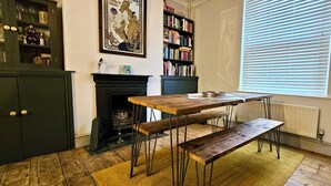 A cozy room with a wooden table and benches, a bookshelf, a fireplace, and a window with blinds. - Glynne Street by Switchback Stays (Cardiff)