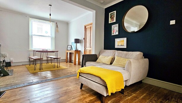 A modern living room with a sofa, a coffee table, and a dining table. There is a large mirror on the wall and a window providing natural light. - Glynne Street by Switchback Stays (Cardiff)