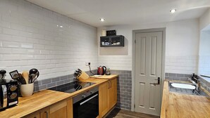A compact kitchen with a black stove, wooden countertop, and a white tiled backsplash. - Glynne Street by Switchback Stays (Cardiff)