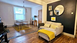 A cozy living room with a sofa, a coffee table, and a TV. There's a staircase to the right and a door leading to another room. - Glynne Street by Switchback Stays (Cardiff)