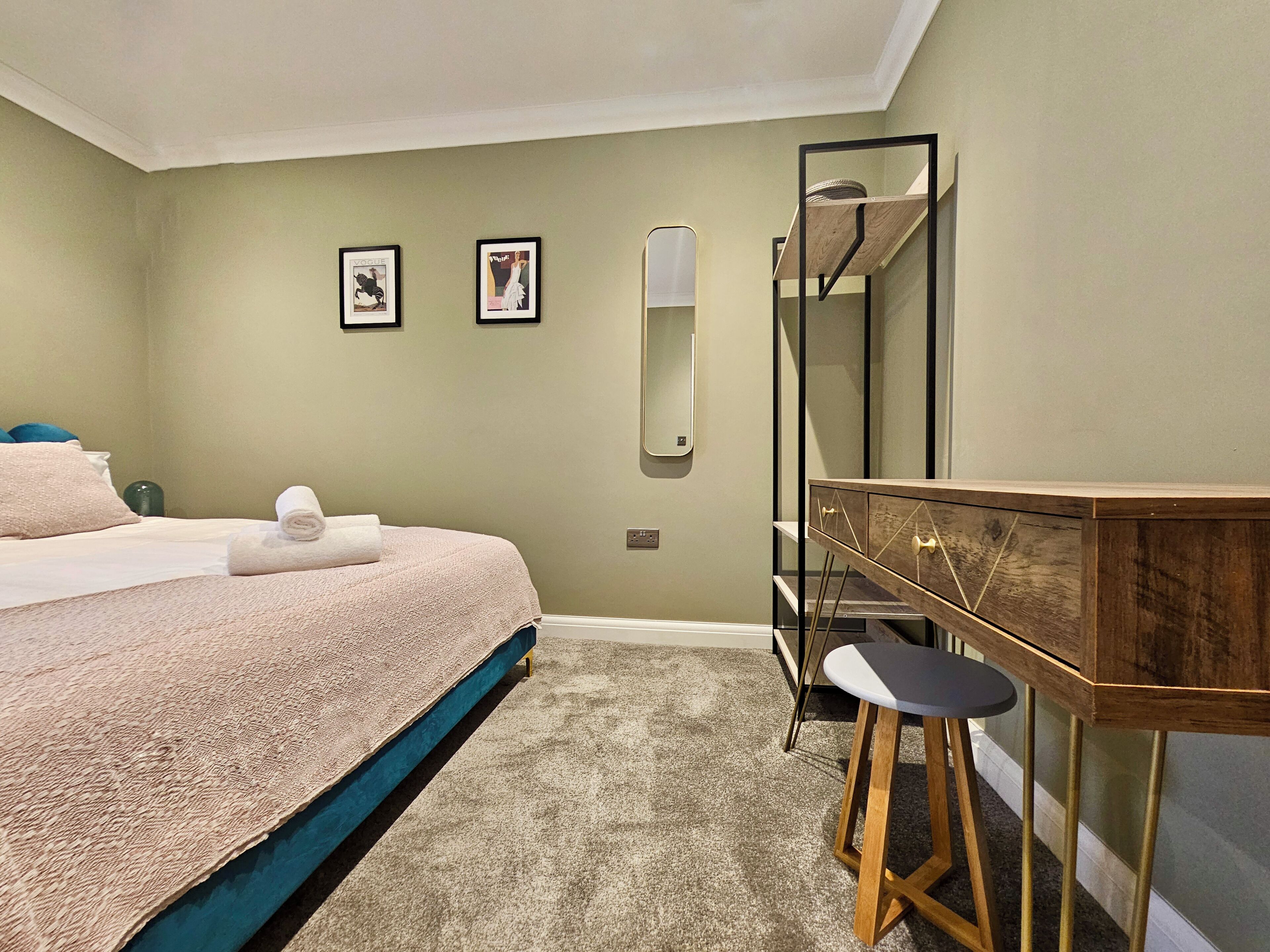 A bedroom with a bed, a desk, and a mirror.