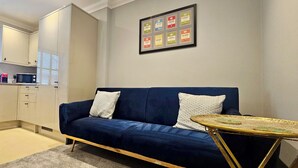 Una sala de estar moderna con un sofá azul, una mesita redonda y una kitchenette al fondo.