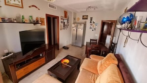 A living room with a TV, sofa, coffee table, and a dining area with chairs and a table. - Orchard Apartment (Lucena)