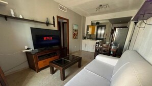 A living room with a flat-screen TV, a sofa, a coffee table, and a kitchen area in the background. - Orchard Apartment (Lucena)