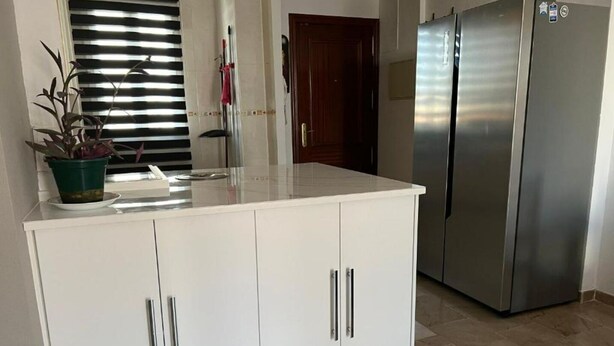 A kitchen with white cabinets, a stainless steel refrigerator, and a potted plant on the counter. - Orchard Apartment (Lucena)