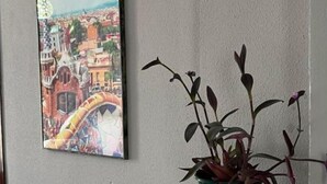 A framed cityscape painting on a wall, a potted plant on a white table, and a plain wall. - Orchard Apartment (Lucena)