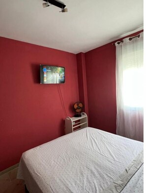 A bedroom with a bed, a wall-mounted TV, a ceiling fan, and a window with curtains. - Orchard Apartment (Lucena)