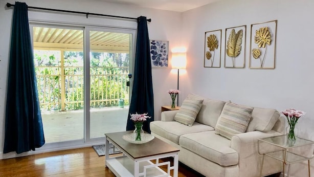 Sala de estar com sofá, mesa de centro e luminária. Há uma porta de vidro deslizante que dá para uma área externa.