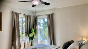 Quarto com cama, ventoinha no teto, janela com cortinas e abajur.