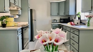 Uma cozinha moderna com armários cinza, uma geladeira de aço inoxidável e um microondas. Há um vaso com flores na bancada.