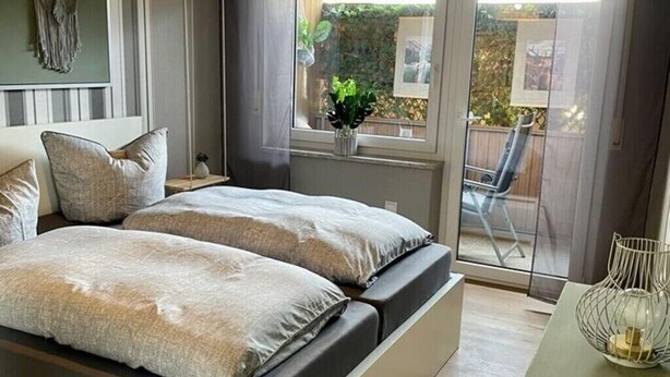 Une chambre moderne avec un grand lit, un luminaire suspendu et une vue sur l’extérieur grâce à une porte-fenêtre coulissante.