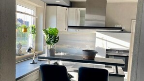 Une cuisine moderne avec des meubles blancs, un plan de travail noir et deux tabourets de bar noirs.