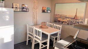 Une cuisine compacte comprenant une table à manger, des chaises, une cuisinière et une étagère murale où sont rangés des livres et un attrape-rêves.