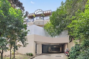A modern building with a covered balcony, a garage, and surrounding greenery.