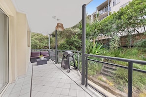 Ein Balkon mit Grill, Sitzgelegenheiten im Freien und Blick auf die grüne Umgebung.