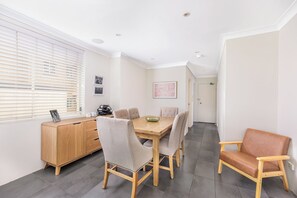 A dining area with a wooden table, six chairs, a wooden cabinet, and a window with blinds.