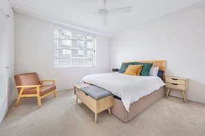 Una camera da letto con un letto, una sedia, un comodino, una panca e una ventola a soffitto.