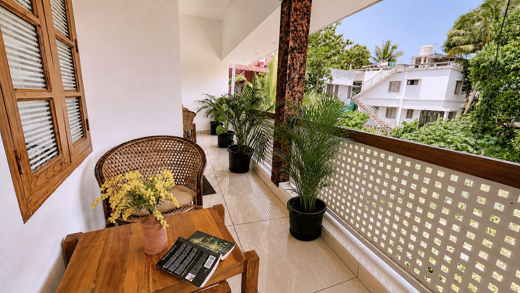 A balcony with a wooden table, chairs, potted plants, and a view of buildings.