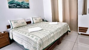 A neatly made bed with a patterned bedspread, a bedside table with a lamp, and a painting on the wall.