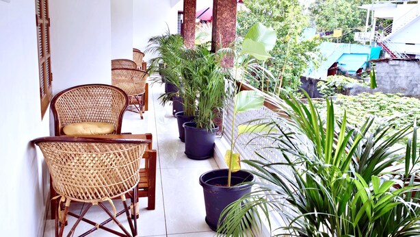 A balcony with wicker chairs, potted plants, and a view of a building and greenery.