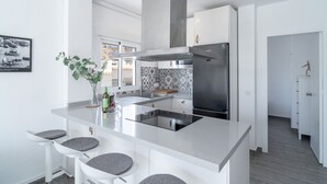 Une cuisine moderne dotée d’un îlot central, d’appareils électroménagers en acier inoxydable et d’un revêtement mural décoratif à motifs géométriques.