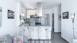 Une cuisine moderne avec des armoires blanches, une hotte de cuisinière en acier inoxydable et un îlot central doté de tabourets de bar.