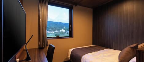 Habitación de hotel con cama, escritorio, silla, televisor y ventana con vista a una montaña y un edificio.