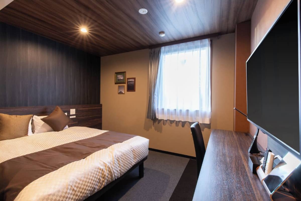 A hotel room with a large bed, a desk with a computer, and a window with curtains.