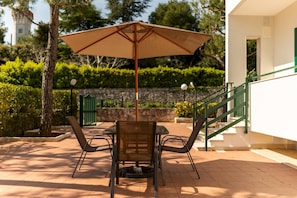 An outdoor patio with a table and chairs, a large umbrella, and a staircase leading to a building.