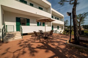 A two-story building with a patio area featuring a table and chairs, a staircase, and a view of the surrounding landscape.