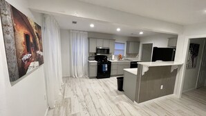 A modern kitchen with white cabinets, a black stove, and a microwave. There is a small island with a sink and a trash can. - The Capitol House (Oklahoma City)