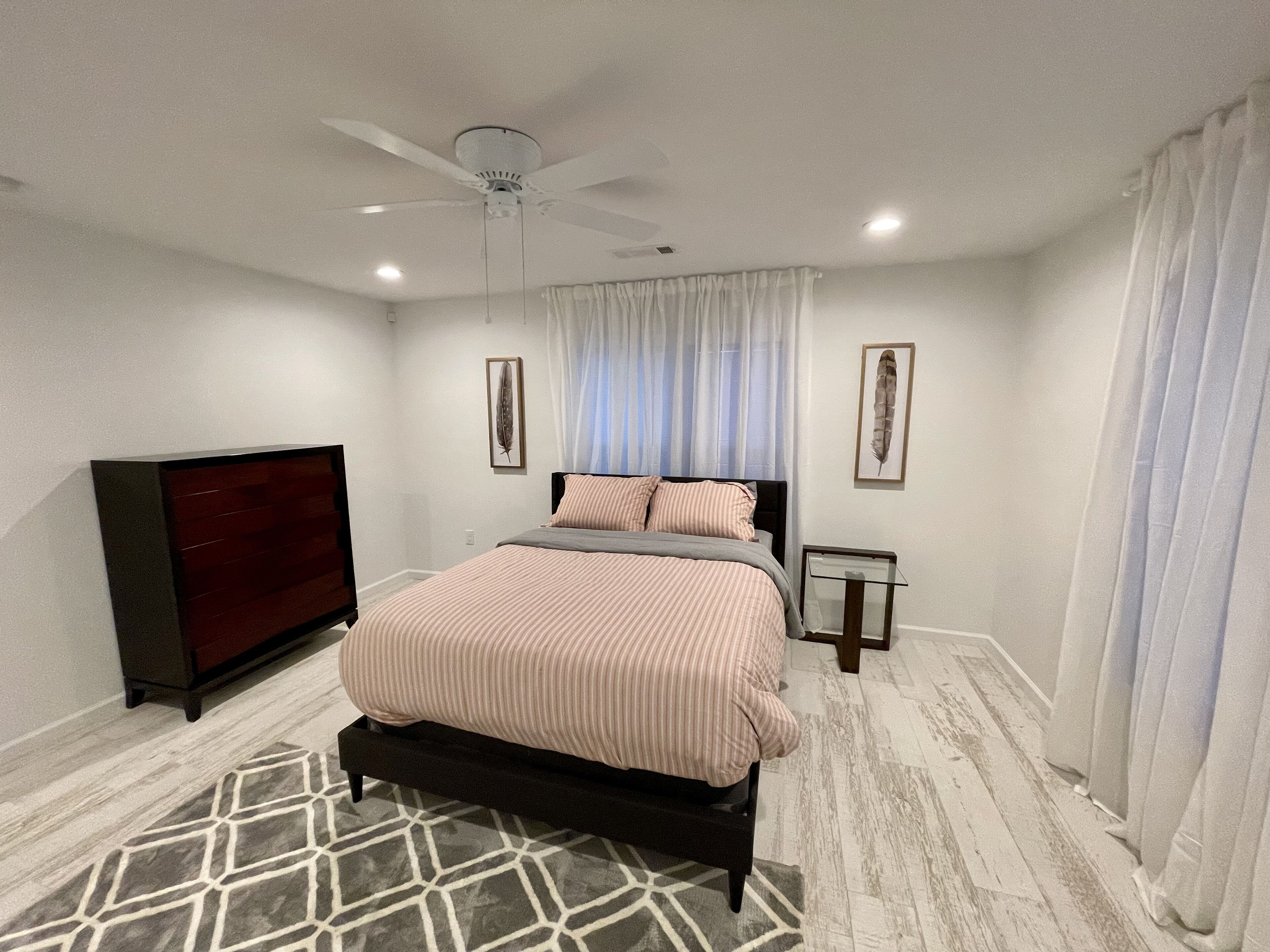Un dormitorio con cama, ventilador de techo, cómoda y alfombra.