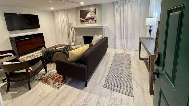A modern living room with a sofa, TV, fireplace, and a ceiling fan. - The Capitol House (Oklahoma City)
