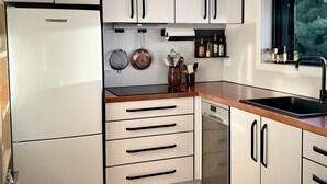Une cuisine moderne avec des meubles blancs, un plan de travail en bois, un luminaire noir suspendu et une fenêtre donnant sur un paysage verdoyant.