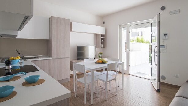 Une cuisine moderne avec des meubles blancs, une table à manger avec des chaises et un panier de fruits posé sur le comptoir.
