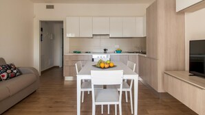Une cuisine moderne avec des meubles blancs, une table à manger avec des chaises et un panier de fruits posé sur la table.