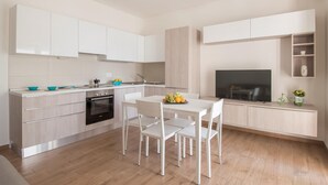 Une cuisine moderne avec des meubles blancs, un four encastré et un coin repas comprenant des chaises et une table, le tout dans des tons blancs.