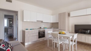 Une cuisine moderne avec des meubles blancs, un coin repas comprenant une table et des chaises blanches, et un téléviseur à écran plat fixé au mur.