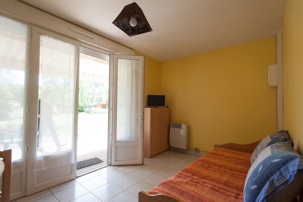 Habitación con cama, televisor, armario y puerta corrediza de vidrio que da a un espacio exterior.