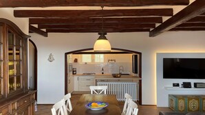 Un coin repas avec une table et des chaises en bois, une cuisine à l’arrière-plan et un téléviseur à écran plat fixé au mur.
