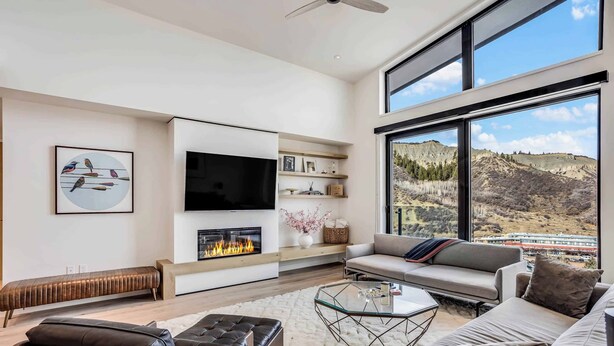 A modern living room with a fireplace, large windows, and a view of a mountainous landscape. - Electric Pass Lodge 604 (Snowmass)