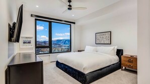 A modern bedroom with a large window, a bed, a bedside table, and a ceiling fan. - Electric Pass Lodge 604 (Snowmass)