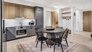A modern kitchen with a built-in oven, a dining table with chairs, and wooden cabinets. - Electric Pass Lodge 604 (Snowmass)