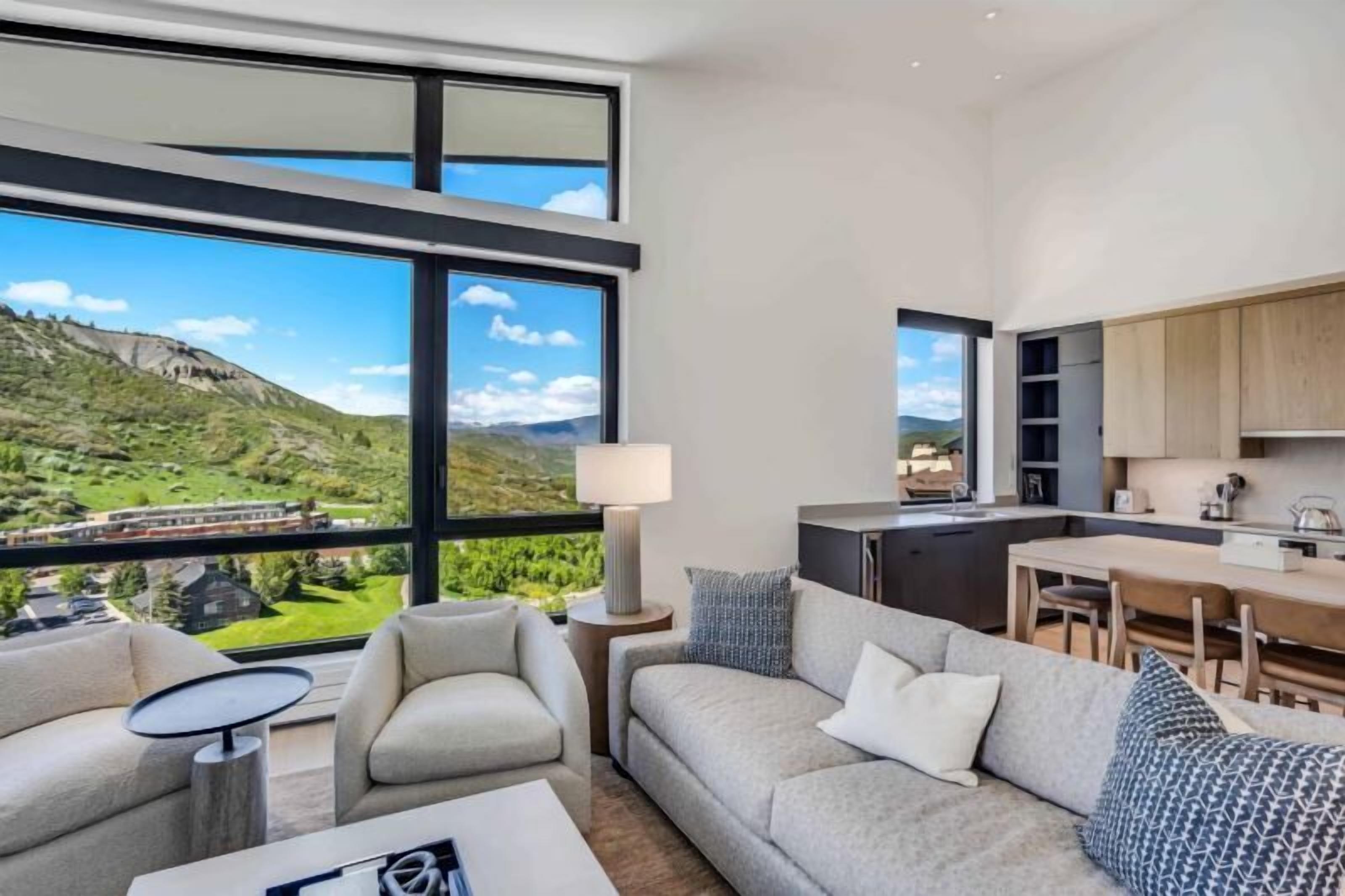 Un moderno salón con un amplio ventanal que ofrece una vista panorámica de un paisaje montañoso.
