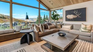 Un salon moderne doté d’une grande fenêtre, d’un plafond en bois et d’un tableau représentant un élan, encadré.