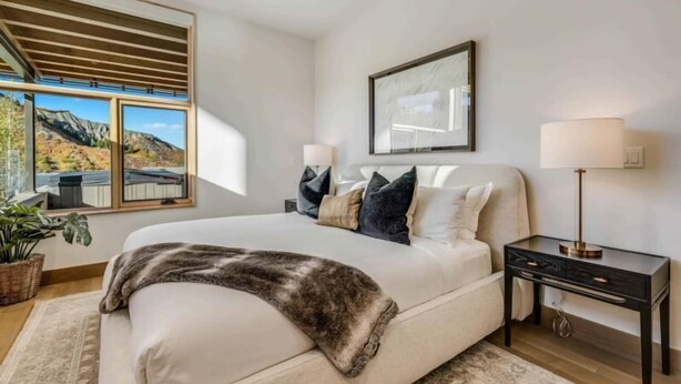 Une chambre avec un grand lit, une table de chevet, une lampe, un tableau encadré au mur et une fenêtre donnant sur la montagne.