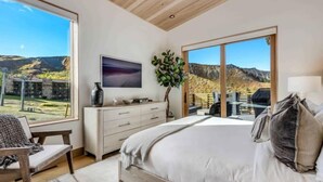 Un dormitorio con una cama grande, un aparador, un televisor y vistas a un paisaje montañoso.